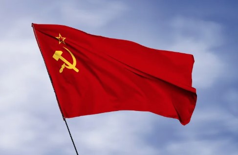 Алый флаг с золотыми серпом, молотом и звездой на фоне голубого неба